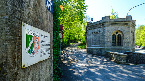 Links im Bild hängt an einer Mauer das Schild für Denkmalschutz, während rechts im Hintergrund das Turbinenhaus zu sehen ist.