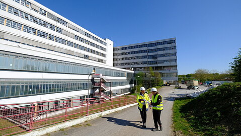 Zwei BLB-Mitarbeiter laufen am Gebäude entlang