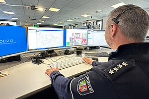 Ein männlich gelesener Polizist beobachtet drei Computer-Monitoren.