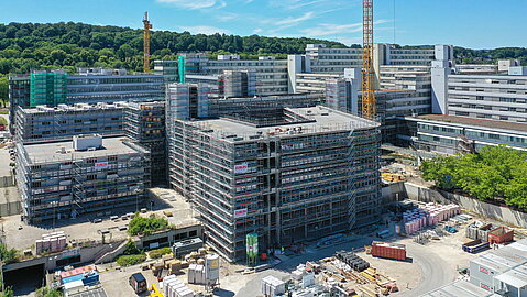 Vor dem Gebäude der Universität Bielefeld ist ein eingerüsteter Neubau zu erkennen, der sich an den Bestand anschließt.