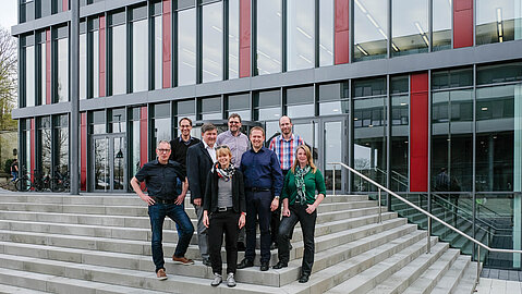 Das achtköpfige Team rund um das Projekt steht auf einem Treppenaufgang vor einem der Neubauten der Paderborner Universität.