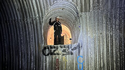 Ein Experte mit Schutzhelm steht in einer bogenförmigen Öffnung in einer mit Graffiti besprühten Metallwand im Inneren.