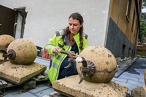 Eine Frau sitzt an großen Sandsteinkugeln und bearbeitet diese. 