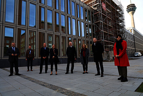 Gruppenfoto vor dem Polizeipräsidium Düsseldorf bei der Einweihung des ersten Bauabschnitts Eine Gruppe von beteiligten Akteuren ist vor dem Polizeipräsidium Düsseldorf zusammengekommen und freut sich über die Einweihung des ersten Bauabschnitts. Im Hintergrund sieht man den fertiggestellten Neubauteil und den eingerüsteten Altbau, der im zweiten Bauabschnitt fertiggestellt wird.