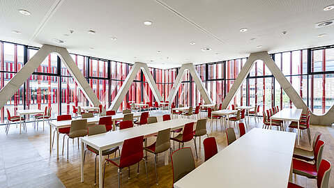Die Mensa der Hochschule mit weißen Tischen und roten Stühlen.