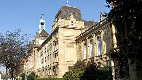 Seitliche Ansicht des denkmalgeschützten Gebäudes der Bezirksregierung Düsseldorf, dass nach dem Vorbild des Reichtagsgebäudes gebaut wurde und neben Figuren, Stuckelemente, gebogene Fenster und eine Steinfassade bietet.