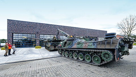 Ein Bergepanzer steht vor einer modernen Halle mit Klinkerfassade.