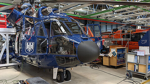 Ein dunkelblauer Hubschrauber der Bundespolizei steht in einer Werkzeughalle. Ein paar Bleche sind entfernt, um an die Maschinenbauteile zu gelangen.