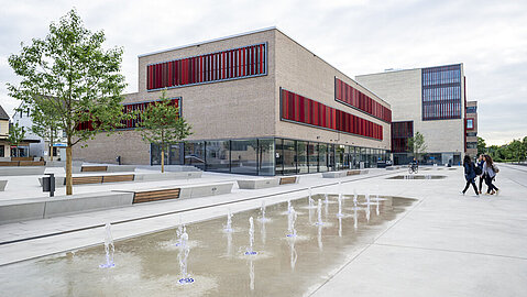 Im Vordergrund ist ein Wasserspiel zu sehen, im Hintergrund stehen die modernen Gebäude der Hochschule Ruhr West.