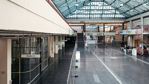 Die zentrale Halle des UHG Bielefeld mit gläsernem Dach, ein zentraler Begegnungs- und Orientierungsort, ist aktuell durch eine Bauzaun-Abtrennung wegen anstehenden Sanierungsarbeiten teilweise gesperrt.