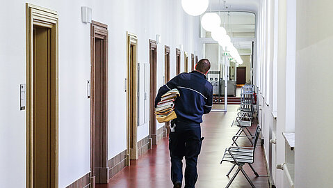 Ein Gerichtsdiener trägt einen Stapel Akten durch den Flur des sanierten Gerichtsgebäudes.