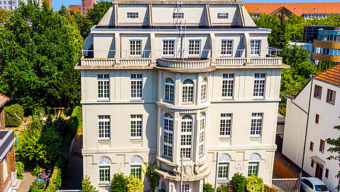 Blick auf eine weiße Villa mit terrassenförmig aufgebauten Dach.