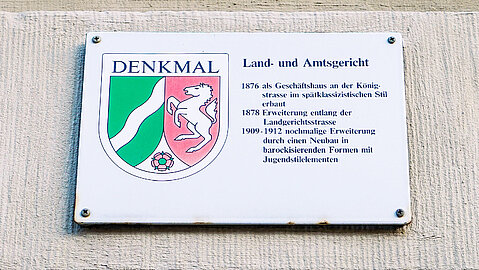 Die Denkmalplakette an der Gebäudefassade des Land- und Amtsgericht Duisburg gibt Aufschluss über die vorherige Nutzung des Gebäudes. 1876 wurde es als Geschäftshaus erbaut, 1878 entlang der Landgerichtsstraße erweitert und von 1909 bis 1912 nochmals erweitert durch einen Neubau.