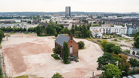 Luftaufnahme von der Ulmer Höh, ehemaliger Sitz der JVA Düsseldorf. Man sieht ein Gebäude umgeben von einem unbebauten Gebiet. Dahinter ist die Skyline der Stadt zu sehen.