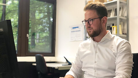 Mutherem Kacar sitzt vor seinem Computer am Schreibtisch. 