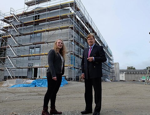 Projektteammitglied Stefanie Hartig und der Minister der Justiz NRW, Peter Biesenbach, vor der eingerüsteten Hafthaus-Baustelle in der JVA Bielefeld-Brackwede. Das Hafthaus ist das erste in Nordrhein-Westfalen, das in Modulbauweise entsteht.