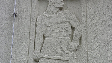 An der Fassade des Gebäudes werden Berufe aus dem Steinbruch dargestellt. Hier ist der Schmied bei seiner Arbeit zu sehen.