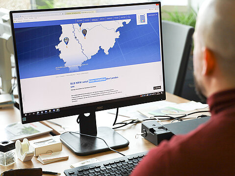 Mann am PC vor Photovoltaik-Sonderseite Auf einem Computer-Bildschirm ist die Sonderseite des BLB NRW zum Photovoltaik-Ausbau zu sehen.