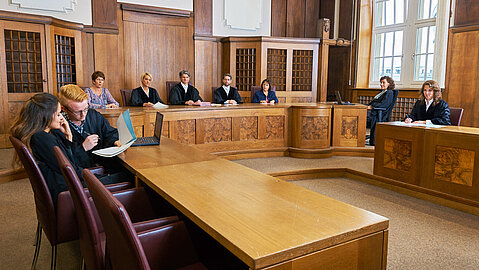 Kläger und Beklagte sitzen vor der vollbesetzten Richterbank in einem der Gerichtssäle im Land- und Amtsgericht Duisburg.