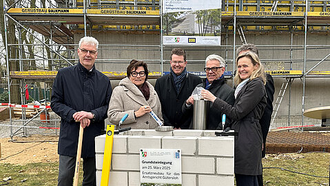 Gruppenbild von der Grundsteinlegung in Gütersloh (v.l.): Mehrere Personen stehen vor einem Baugerüst an einer gemauerten Viereck, um die Zeitkapsel dort einzulegen.