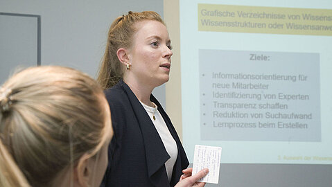 Eine Studierende der FH Dortmund steht seitlich zur Präsentation mit einer Karte in der Hand.