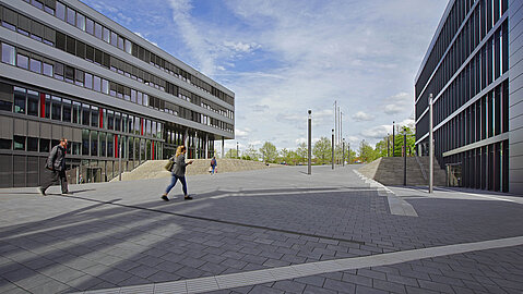 Zwischen den Universitätsgebäuden führt ein asphaltierter Weg, der auch ein Blindenleitsystem hat. Rechts und Links vom Weg befinden sich Treppenaufgänge zu den Eingängen der Gebäude I und Q.